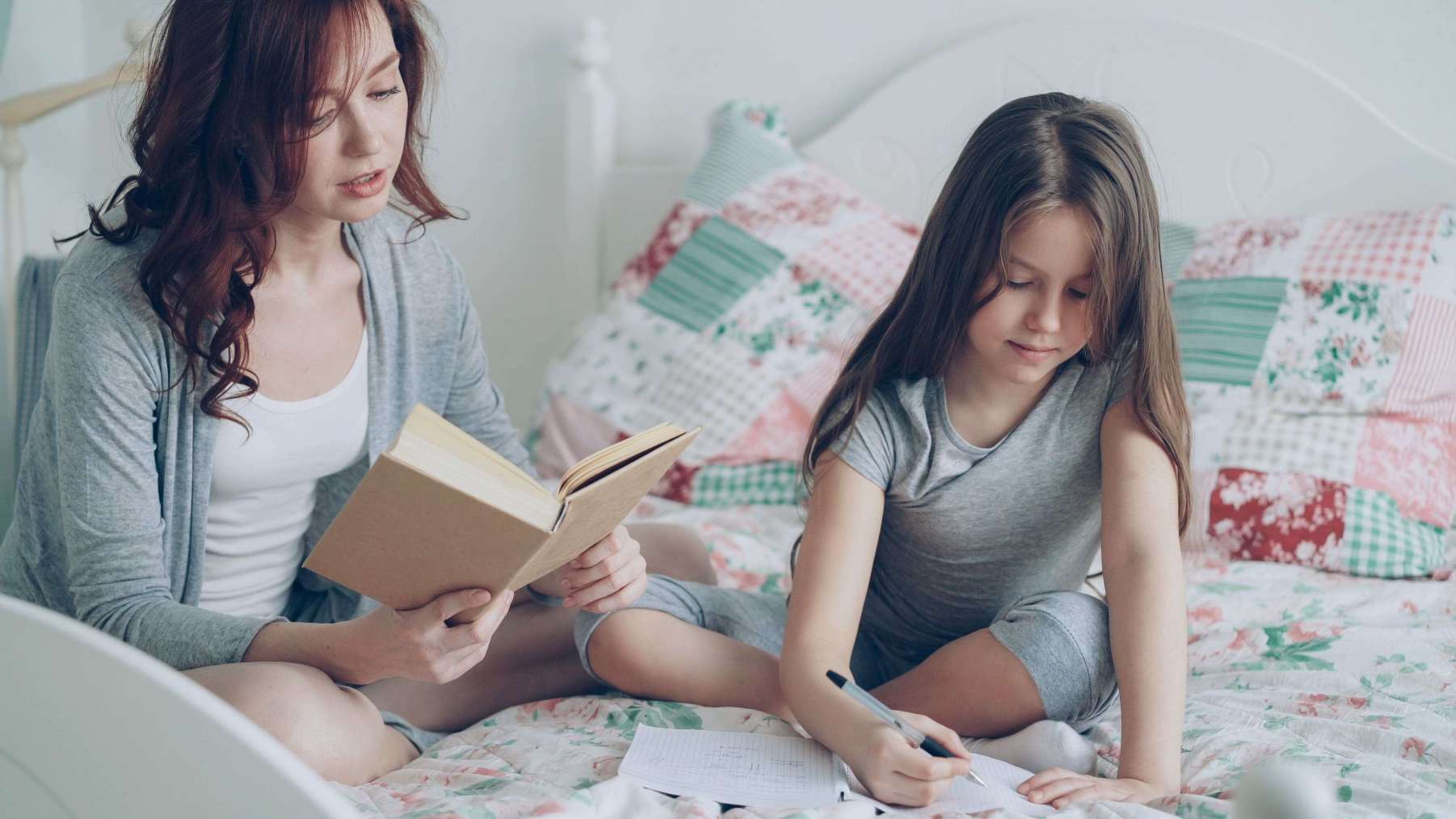 Mère lisant un livre avec sa fille qui écrit dans un cahier